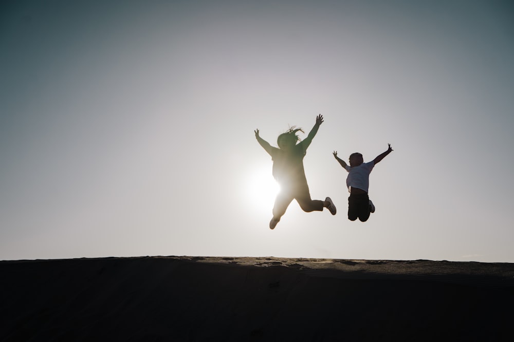 man in black shirt and white pants jumping on brown sand during daytime