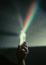 Close-up of hands gently holding a small prism refracting rainbow light.