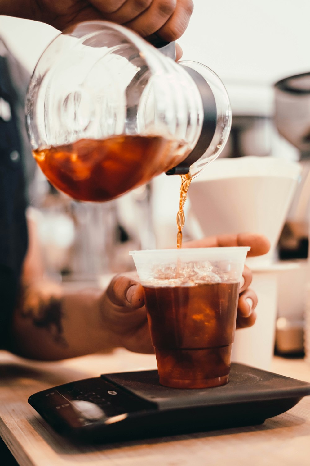 person pouring brown liquid on clear drinking glass