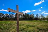 An old wooden cross standing tall among golden wheat under a blue sky.