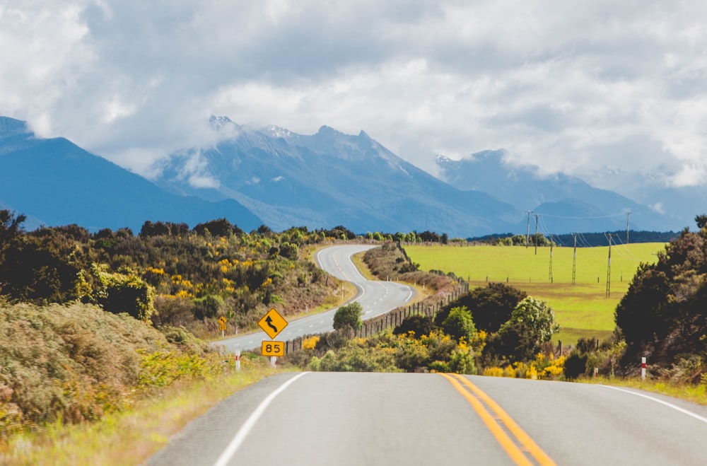 gray concrete road near green trees and mountains during daytime