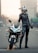 A person dressed in black leather motorcycle gear stands confidently beside a sleek sport bike on an empty urban street. The motorcycle features a distinctive design with bold graphics, and the rider is wearing a full-face helmet.