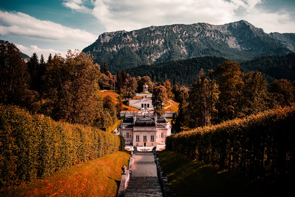 white concrete building near green trees and mountain under blue sky during daytime