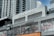 A modern commercial building featuring various business establishments, including a cinema and a fitness studio. The facade displays signage for Cinemark and Trufusion, with glass windows showing images related to fitness activities. Above the establishments are residential or office high-rise structures with numerous balconies.