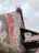 A mural on a building wall features a large red and white design with artistic patterns and the number 190 prominently displayed. The word 'Monty's' is written in bold white letters, contrasting with a red background. Below the mural, there is an awning indicating a business establishment, suggesting it could be a restaurant or shop. Some foliage is visible at the bottom left of the image, under a cloudy sky.