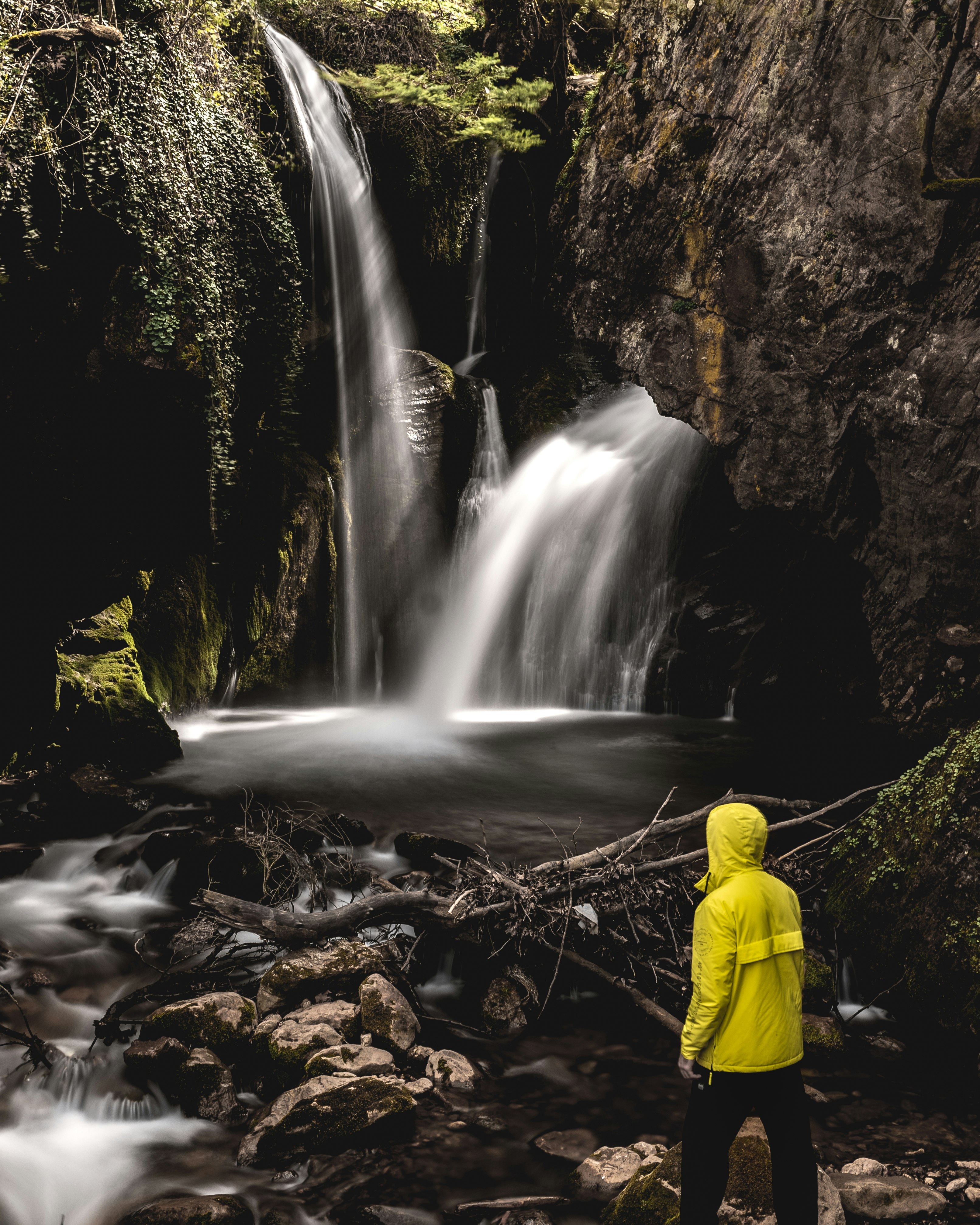 man in yellow jacket standing in front of waterfalls during daytime