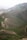 A serene landscape featuring rolling hills covered with patches of green grass and bare earth. A herd of livestock, possibly sheep or goats, is gathered near the center, grazing on the slopes. The scene is expansive, with intricate patterns formed by natural contours and pathways meandering through the terrain.