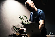 Social media manager working on a laptop surrounded by plants and warm ambient lighting.