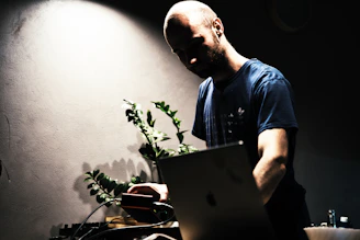 Social media manager working on a laptop surrounded by plants and warm ambient lighting.
