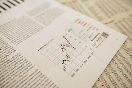 A financial report is laid out with an intricate chart showing data trends over multiple years. Surrounding text appears to be in a newspaper format, with graphs and tables prominently displayed. The focus is on a detailed line graph illustrating fluctuations.