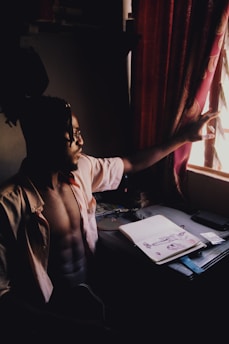 Portrait of Breno Massena, a writer from Rio de Janeiro, sitting by a window with a notebook and pen.