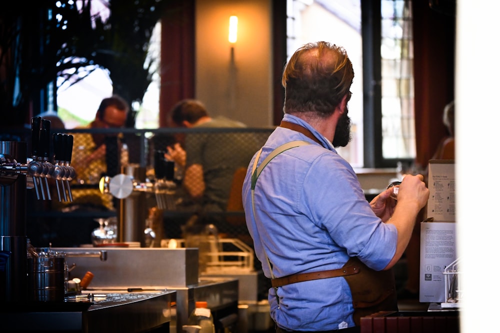 man in blue long sleeve shirt and blue denim jeans standing near table