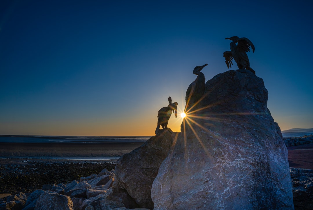 man in yellow jacket and black pants standing on rock formation near sea during daytime