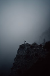 person standing on cliff during foggy weather