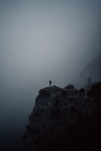 person standing on cliff during foggy weather