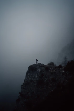 A shadowy figure standing at the edge of a foggy abandoned town at dusk.