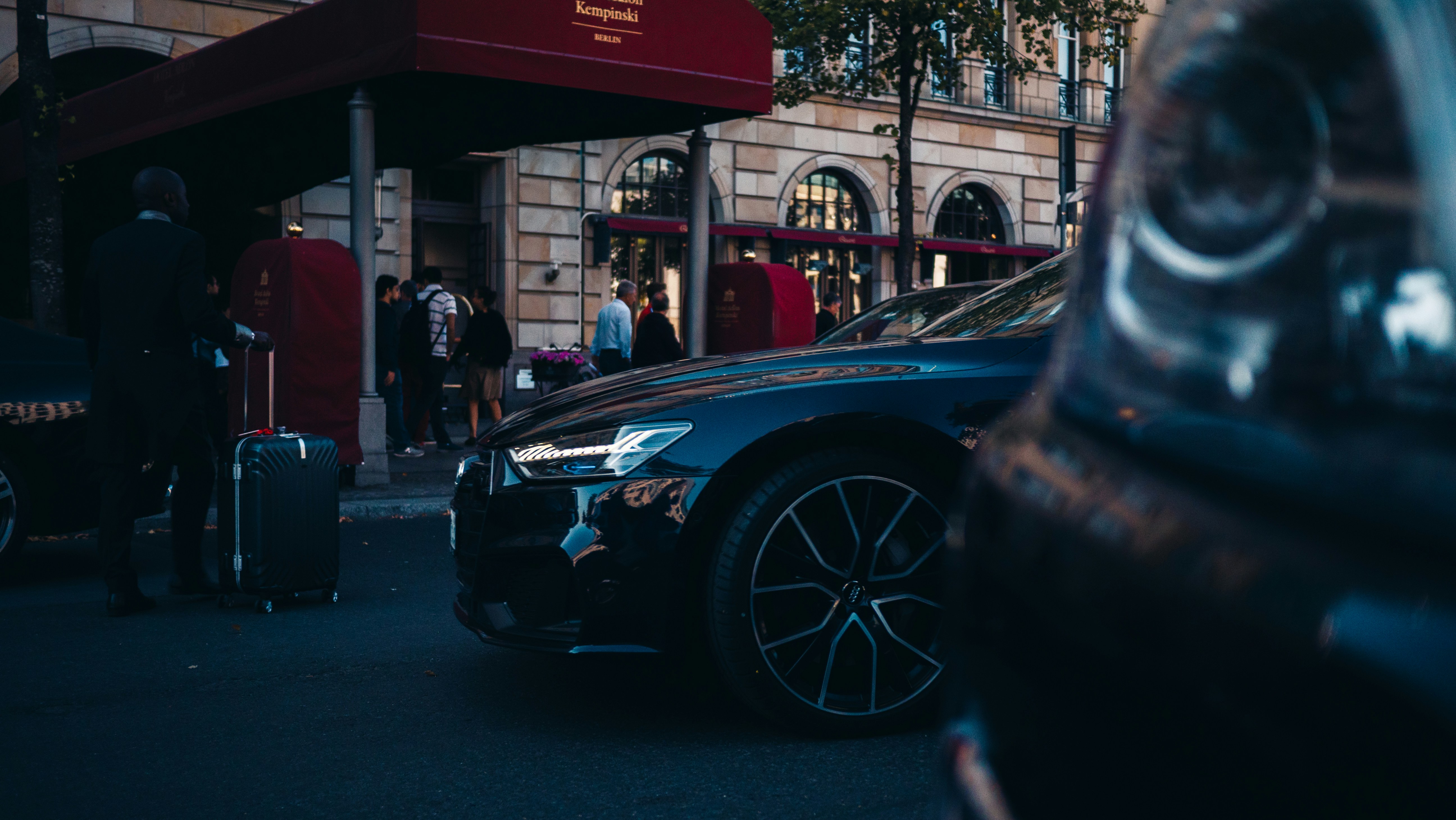 A valet stands with luggage by a luxury car at a hotel.