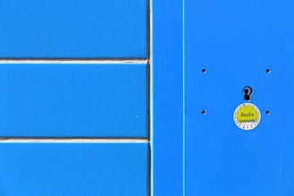A bright blue textured surface with a vertical light blue stripe on the right. The center features a round, yellow sticker with text and a keyhole cutout.