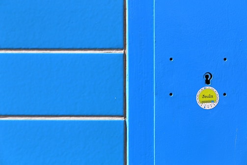 A bright blue textured surface with a vertical light blue stripe on the right. The center features a round, yellow sticker with text and a keyhole cutout.