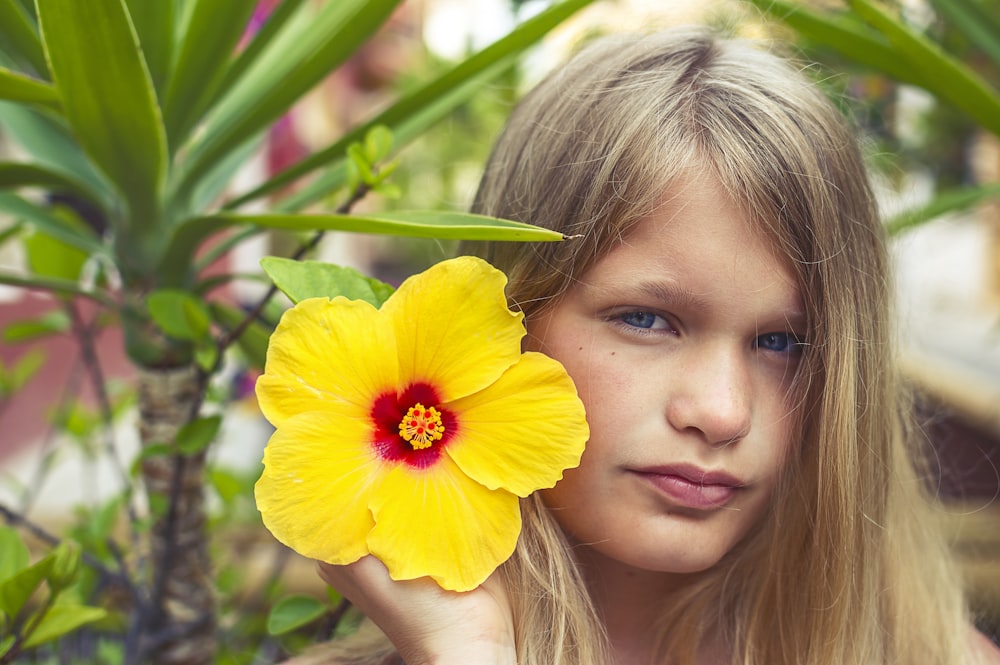 menina que segura a flor amarela durante o dia