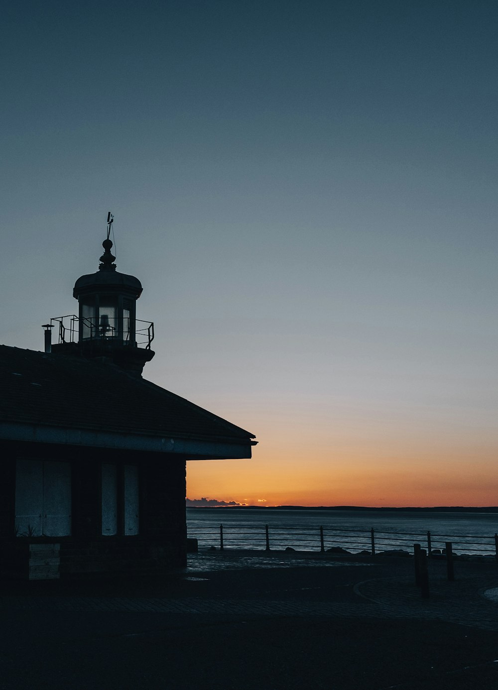 silhouette of house near body of water during sunset