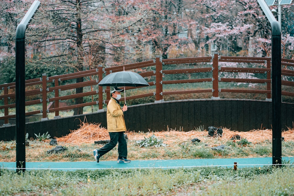 donna in cappotto marrone che tiene l'ombrello che cammina sul sentiero