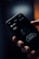 A hand is holding a smartphone with a dark-themed screen displaying a shopping cart interface. The screen shows text reading 'Can't see anything here...' and a button labeled 'Explore our products'. The background appears blurry with warm, soft lighting.