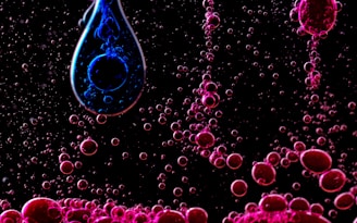 A black background with small bubbles of pink and a larger droplet containing swirling blue. The bubbles appear suspended or rising, creating a dynamic, almost abstract visual.