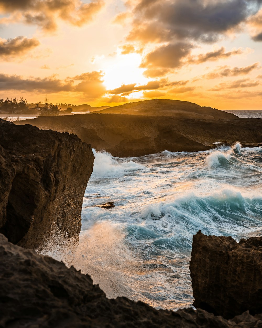 Meereswellen stürzen während des Sonnenuntergangs auf braune felsige Küste