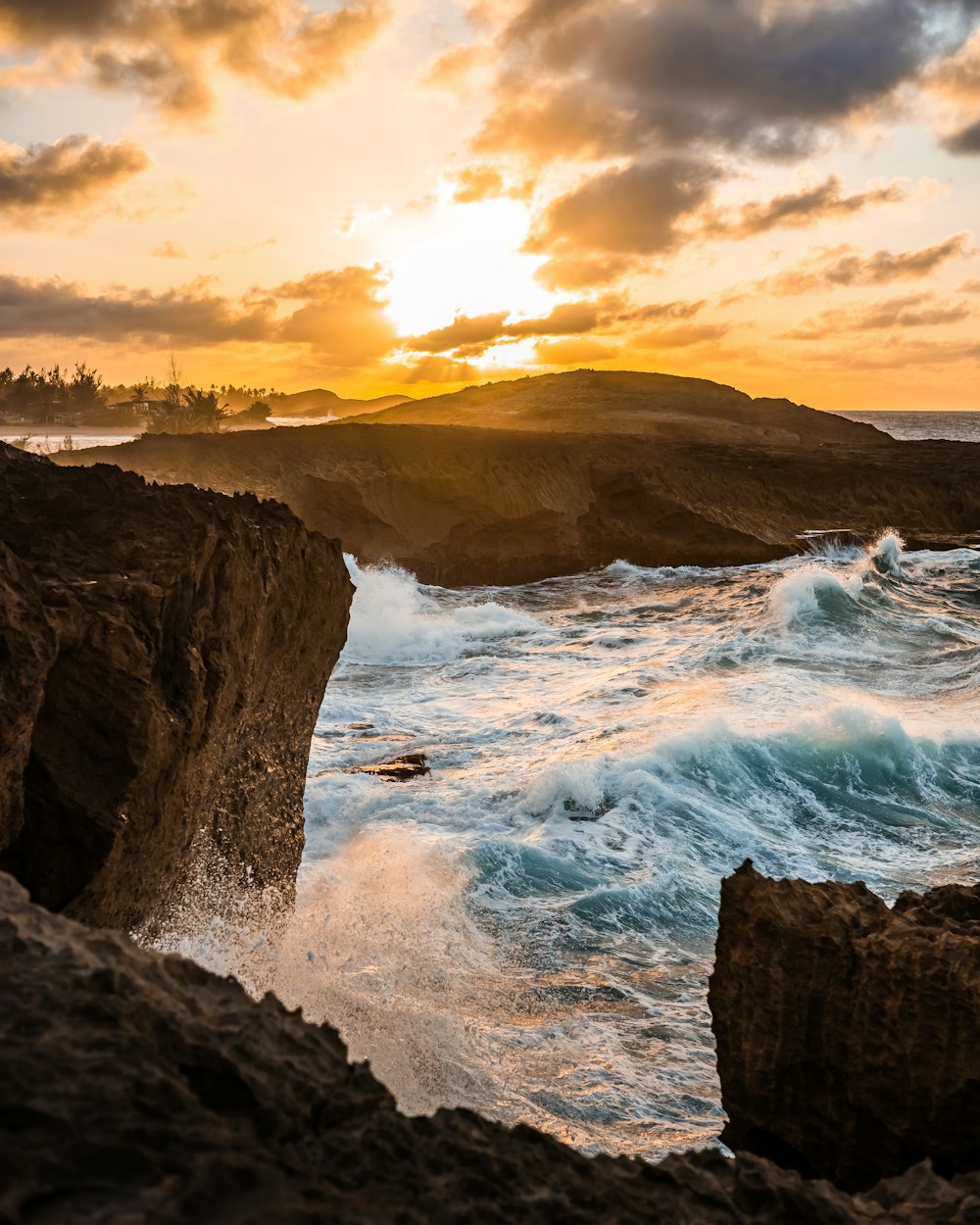 ocean waves crashing on brown rocky shore during sunset
