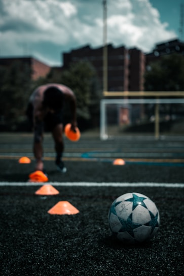 A focused young soccer player dribbling a ball through cones on a sunny training field.