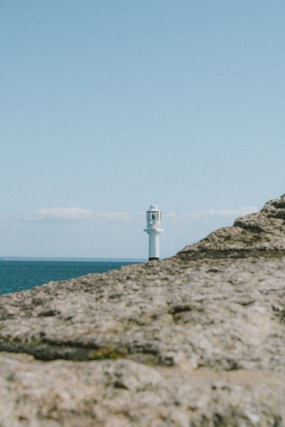 white lighthouse on gray rock formation near body of water during daytime