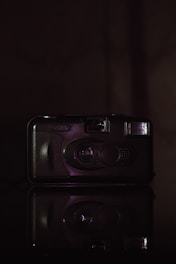 Black and white photograph of a vintage camera and cassette tape, glowing faintly on a dark background.