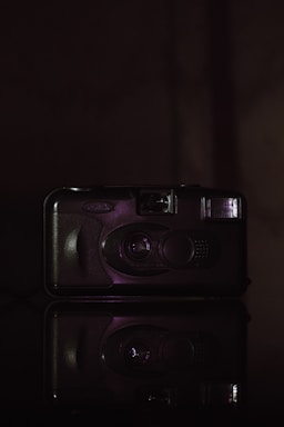 Black and white photograph of a vintage camera and cassette tape, glowing faintly on a dark background.