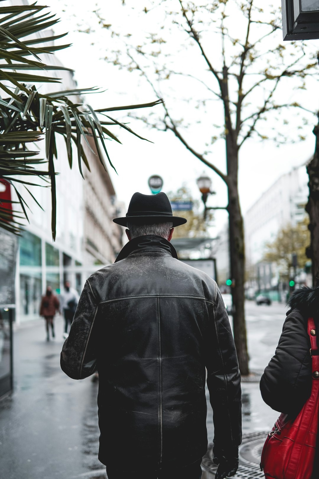 man in black leather jacket standing near people walking on sidewalk during daytime