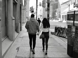 A candid shot of a couple walking hand-in-hand along a charcoal-colored urban street bathed in late afternoon light.