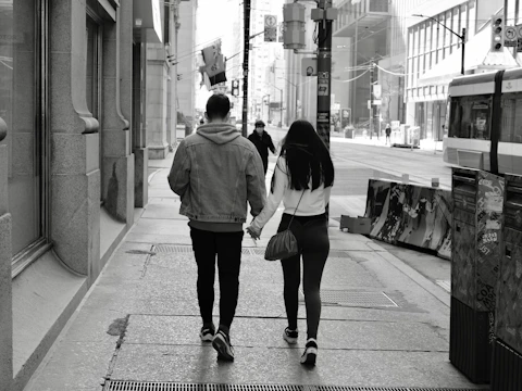 A candid shot of a couple walking hand-in-hand along a charcoal-colored urban street bathed in late afternoon light.