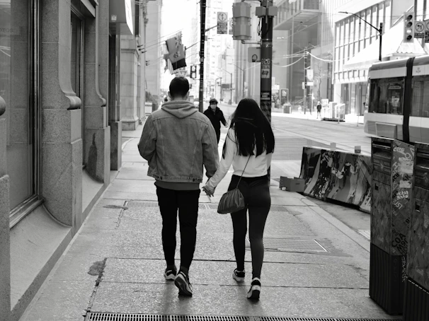 A candid portrait of a couple walking hand-in-hand along a charcoal-hued urban street.
