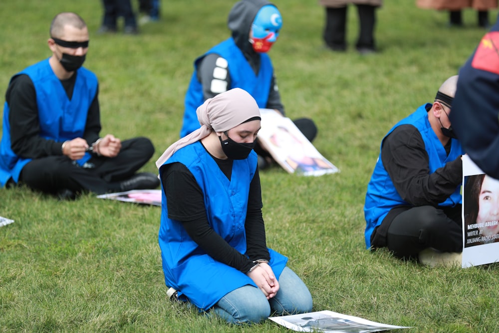 woman in blue jacket and blue denim jeans sitting on green grass field during daytime