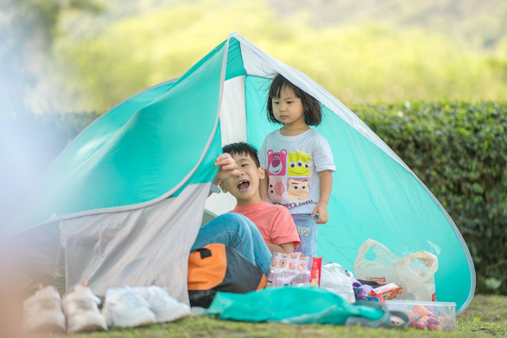 girl in gray crew neck t-shirt sitting on blue and red tent during daytime