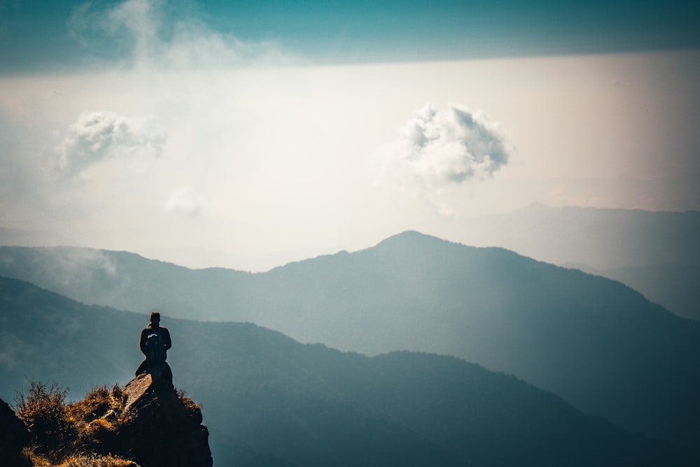 Hombre sentado en la roca en la cima de la montaña durante el día