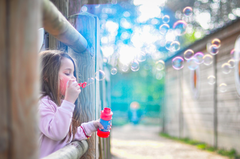 girl in pink jacket blowing bubbles during daytime