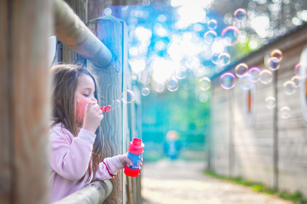 fille en veste rose soufflant des bulles pendant la journée