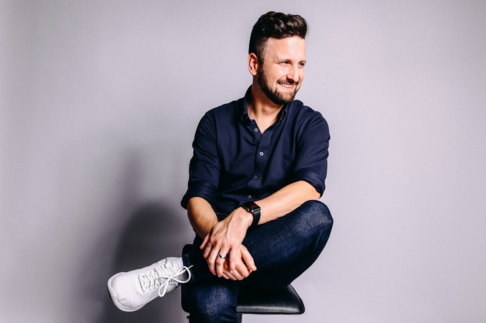 man in black dress shirt and blue denim jeans sitting on black chair