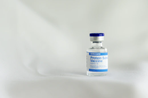 Close-up of a scientist in a lab coat examining a vaccine vial under soft blue lighting.