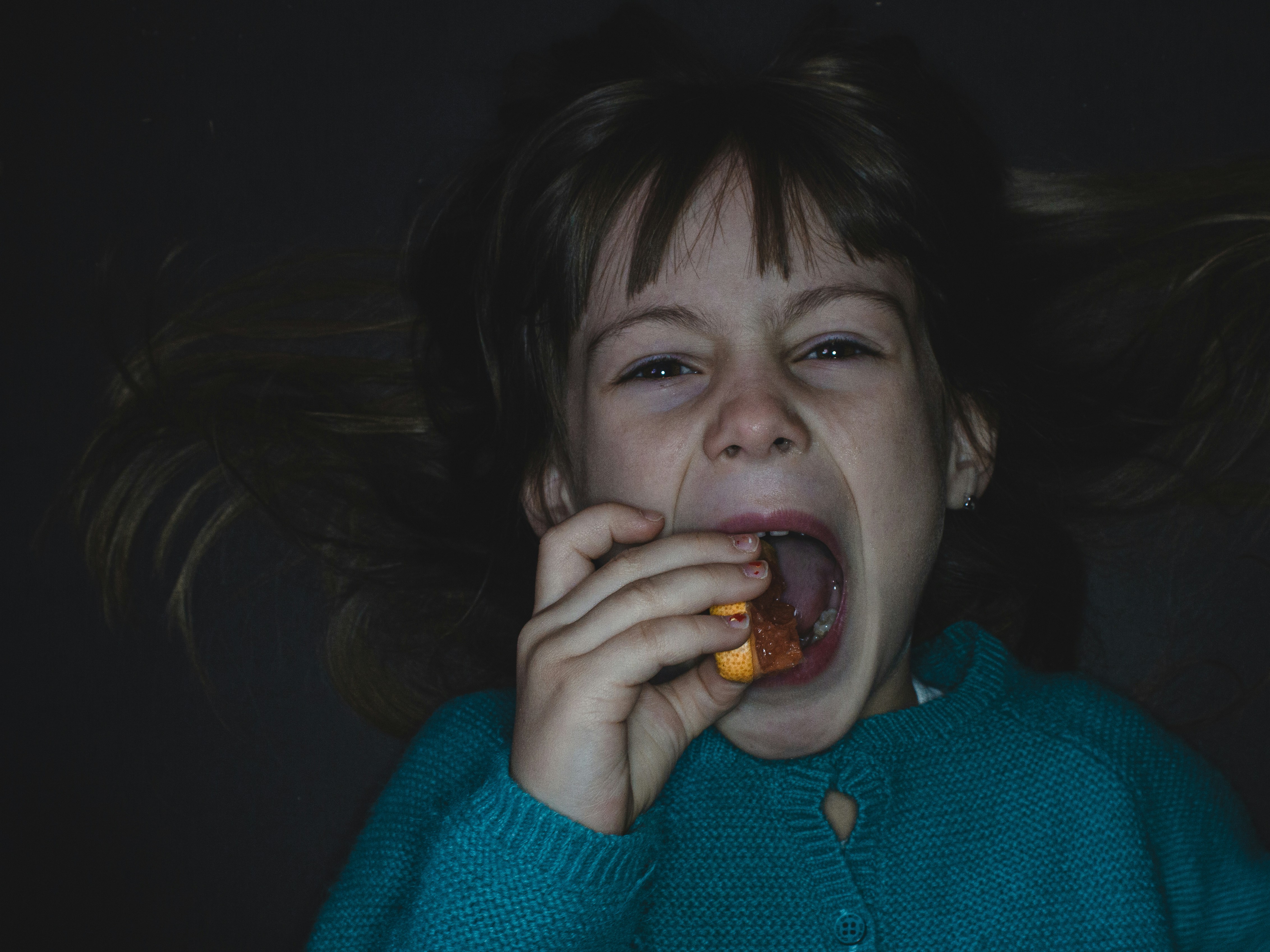 girl in blue sweater eating orange fruit