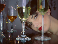 A woman’s face partially hidden behind a glass of red wine, her eyes reflecting stories untold.