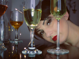 A woman’s face partially hidden behind a glass of red wine, her eyes reflecting stories untold.