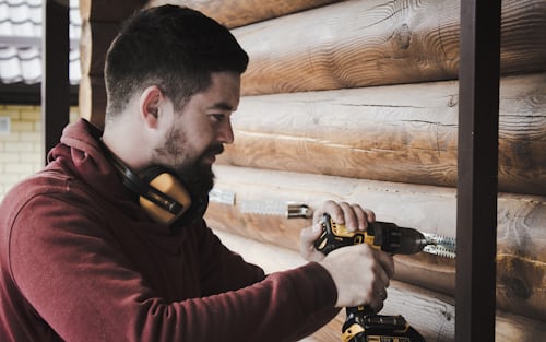 A man using a drill machine to drill a hole in a wooden wall