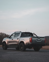 A shining silver pickup truck loaded with camping gear on a forest road.
